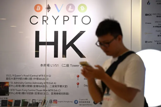 رجل يستخدم هاتفه الجوال أمام بورصة للعملات المشفرة في هونغ كونغ (أ.ف.ب)