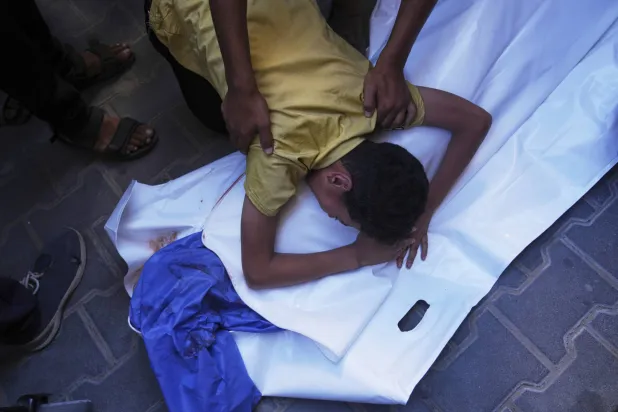 طفل فلسطيني يحتضن جثمان صديقه عبد الله أحمد البالغ من العمر 12 عاماً الذي قُتل في غارة إسرائيلية استهدفت نقطة توزيع مياه الشرب بمستشفى العودة بالنصيرات (أ.ب)