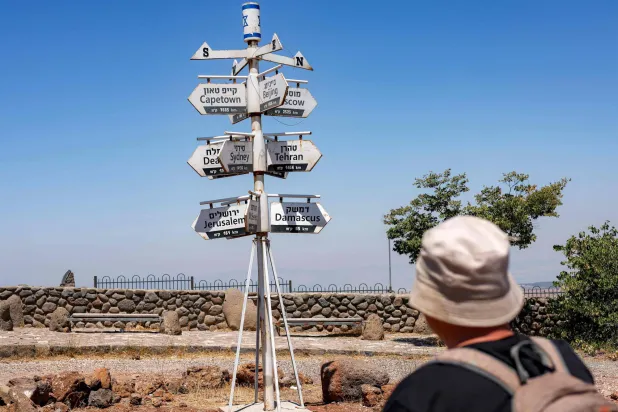 لافتة تشير إلى اتجاهات مدن في أنحاء العالم تسرد مسافاتها من نقطة مراقبة سياحية في موقع للجيش الإسرائيلي على جبل بنتال (تل الغرام) في مرتفعات الجولان المحتلة (أ.ف.ب)