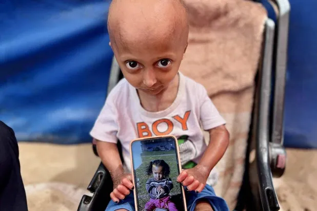 الطفلة حلا الهنادي تمسك هاتفاً عليه صورتها قبل اشتداد المرض (المصوِّر من غزة عمرو طبش عبر «إنستغرام»)