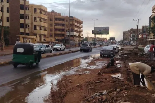 مواطن يحاول تصريف المياه من أمام مسكنه في مدينة أم درمان (الشرق الأوسط)