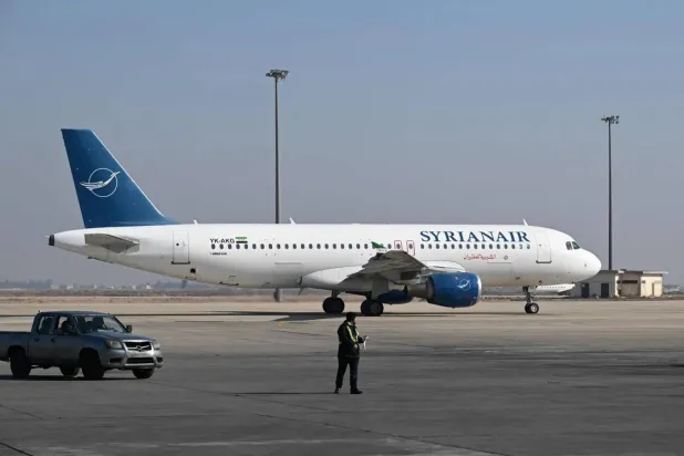 An airport worker walks on the tarmac next to a Syrian Air plane at the Damascus International Airport on January 7, 2025. (Photo by LOUAI BESHARA / AFP)