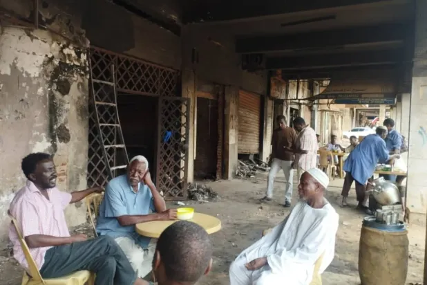 Hartum'daki bir çarşıda yanmış dükkanlarının önünde oturan dükkan sahipleri (Şarku’l Avsat)