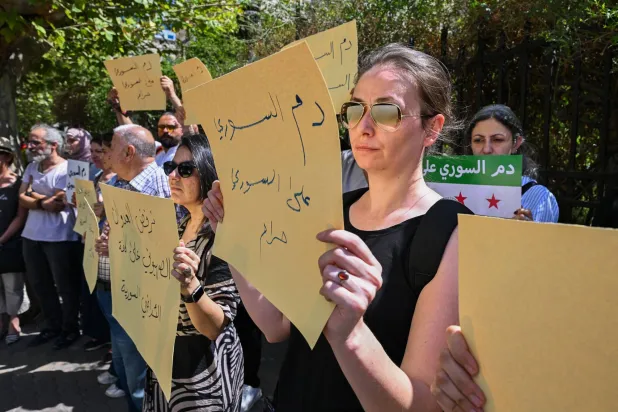 سوريون يرفعون لافتات خلال مظاهرة احتجاجية على الاشتباكات والضربات الإسرائيلية في السويداء أمام البرلمان في دمشق (أ.ف.ب)