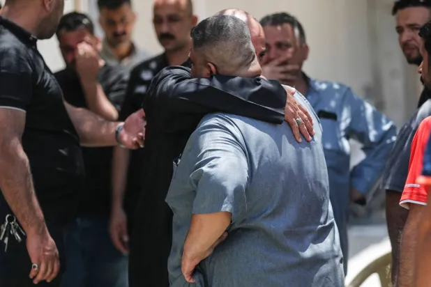 أقارب ضحايا حريق المركز التجاري في الكوت يحتضن بعضهم بعضاً خارج قسم الطب الشرعي بالمدينة (أ.ف.ب)