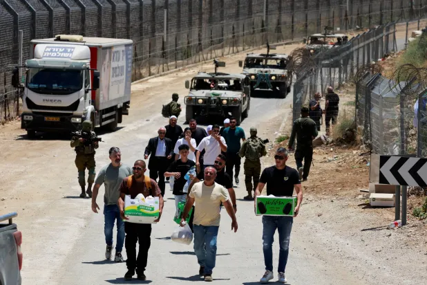  الجيش الإسرائيلي يرافق مجموعة من الدروز السوريين أثناء عودتهم سيراً على الأقدام من مجدل شمس إلى الجولان المحتل الخميس (رويترز)