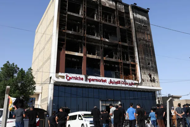أشخاص يتجمعون بجوار مركز تجاري دمر خلال حريق هائل اندلع ليلاً وأودى بحياة العشرات في الكوت بمحافظة واسط بالعراق (رويترز)