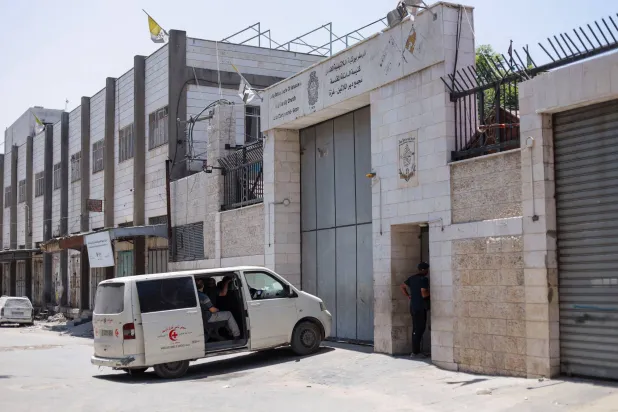 أشخاص يجلسون داخل مركبة أمام كنيسة العائلة المقدسة بغزة التي تضررت جراء قصف إسرائيلي (رويترز)