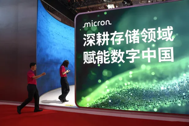 أفراد من فريق العمل يمرون أمام جناح شركة «ميكرون» الأميركية لتصنيع ذاكرة الكومبيوتر خلال معرض الصين الدولي الثالث لسلسلة التوريد في بكين (إ.ب.أ) 