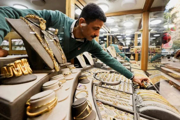 عامل بمتجر للذهب ينسق معروضاته في واجهة المحل (رويترز)