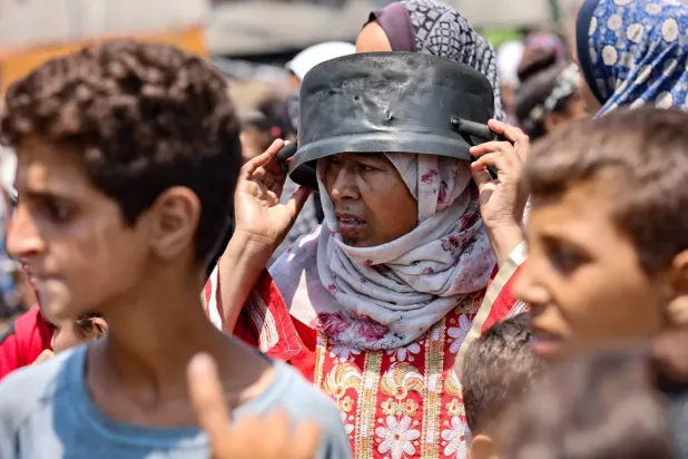 Gazze Şehri'ndeki bir yiyecek dağıtım noktasında bekleyen yerinden edilmiş bir Filistinli kadın, kavurucu güneşten korunmak için tencereyi başına başına koyuyor (AFP)