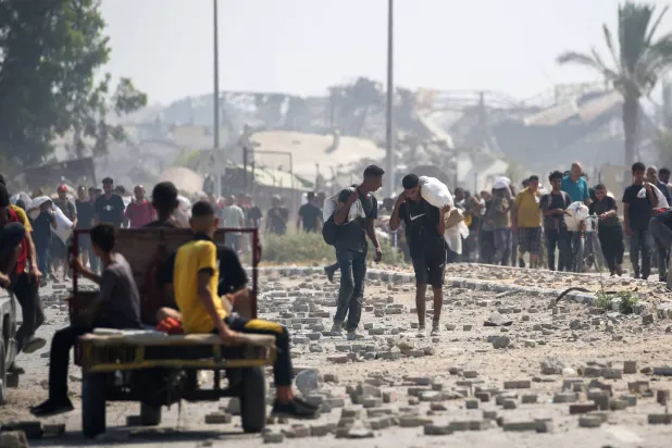 فلسطينيون نازحون في مخيم النصيرات للاجئين يحملون طرودًا غذائية ومواد أخرى تمكنوا من الحصول عليها من نقطة توزيع مساعدات في ما يسمى "ممر نتساريم" في وسط قطاع غزة (أ.ف.ب)