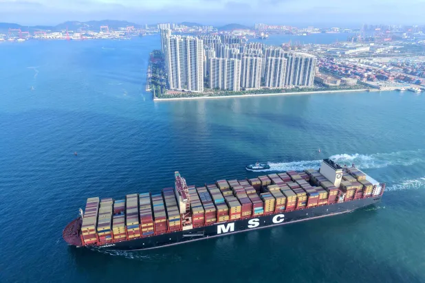 سفينة حاويات تبحر بالقرب من مبانٍ في تشينغداو في مقاطعة شاندونغ شرق الصين (أ.ف.ب)