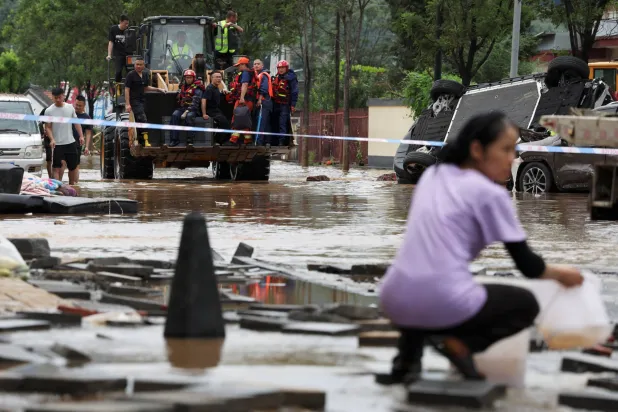 عمال الإنقاذ يركبون رافعة أمامية أثناء شق طريقهم عبر طريق مغمور بالمياه خلف خط الطوق بعد هطول أمطار غزيرة في منطقة مييون ببكين - الصين (رويترز)