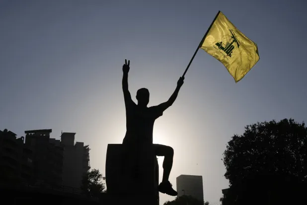 A Hezbollah supporter holds up a Hezbollah flag in front of the headquarters of the UN Economic and Social Commission for Western Asia (ESCWA) in Beirut, Lebanon, Saturday, July 26, 2025, during a demonstration against the Israeli war and what they say is the starvation of civilians in the Gaza Strip. (AP Photo/Bilal Hussein)