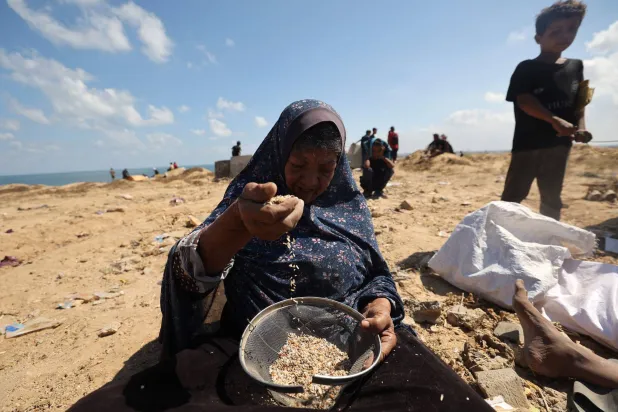 سيدة فلسطينية تبحث عن البقوليات في وسط الرمل في موقع شهد إنزالاً جوياً في مخيم النصيرات في غزة (أ.ف.ب)