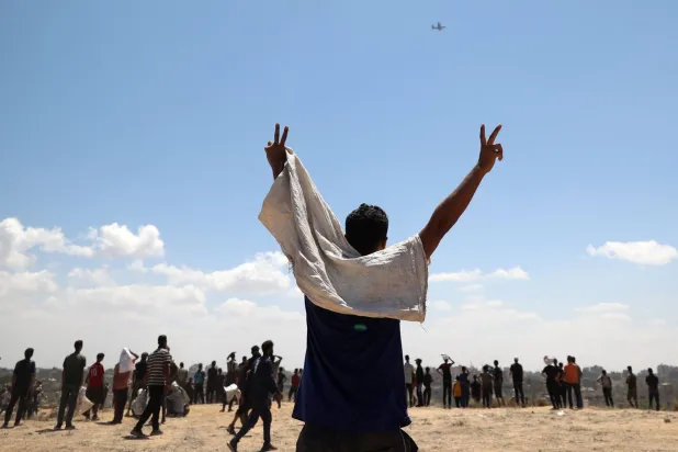 فلسطيني يلوح لطائرة تحمل مساعدات إنسانية فوق النصيرات بوسط قطاع غزة يوم الثلاثاء (أ.ف.ب)