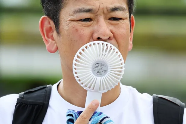 مواطن يستخدم مروحة محمولة للتكيف مع موجة الحر في هيروشيما باليابان (رويترز)