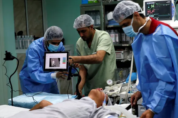 A patient lies on a bed as a technician (L) adjusts a screen before the start of a Proximie surgery, with doctor Ghassan Abu Sitta in Beirut guiding Palestinian surgeon Hafez Abu Khousa in the operating room at Al Awda Hospital in the northern Gaza Strip April 30, 2016. REUTERS/Suhaib Salem