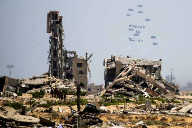  فلسطينيون يشاهدون طرود مساعدات تُلقى من الجو وسط الدمار في منطقة النصيرات وسط غزة أمس (أ.ف.ب)