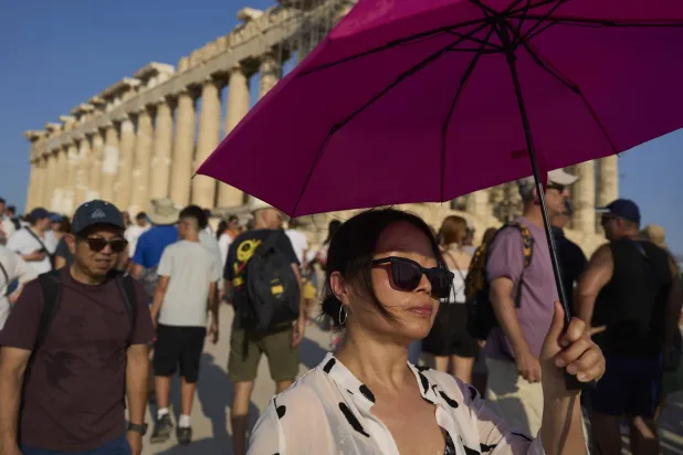 سائحة تحمل مظلة لحماية نفسها من الشمس بينما تسير هي وآخرون أمام معبد البارثينون الأثري على تلة الأكروبوليس خلال موجة حر في أثينا 25 يوليو 2025 (أ.ب)