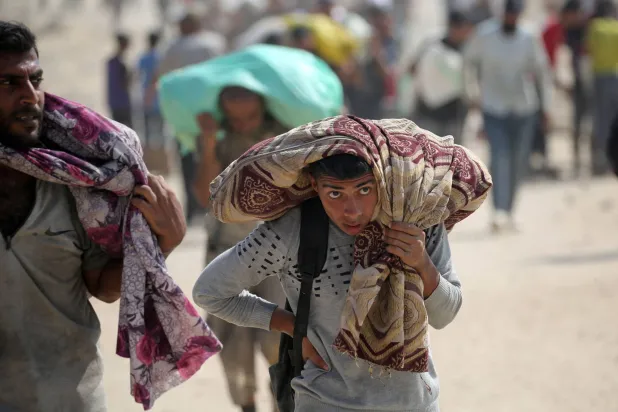 فلسطينيون يحملون أكياساً من القماش أثناء عودتهم من نقطة توزيع مساعدات على طريق صلاح الدين بالقرب من مخيم النصيرات للاجئين في وسط قطاع غزة - 2 أغسطس 2025 (أ.ف.ب)