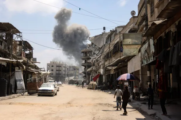 فلسطينيون يراقبون تصاعد عمود من الدخان خلال غارة إسرائيلية على حي الزيتون جنوب مدينة غزة (أ.ف.ب)