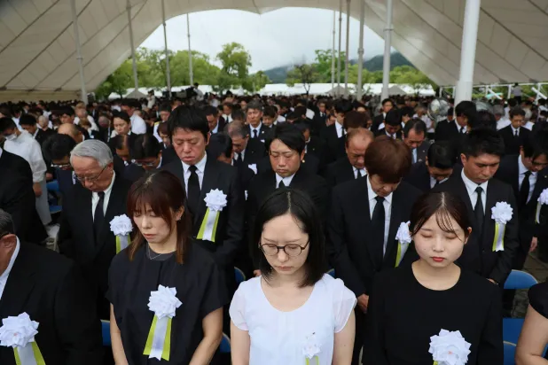 أشخاص يشاركون في دقيقة صمت خلال حفل التأبين السنوي للضحايا بحديقة السلام في ناغازاكي (أ.ف.ب)
