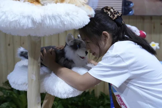 يحمل أحد الزوار حيواناً أليفاً روبوتياً في مؤتمر الروبوتات العالمي لعام 2025 في بكين (أ.ب)