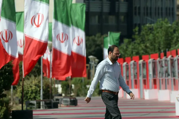 شخص يمشي بجانب الأعلام الإيرانية في أحد شوارع طهران (إ.ب.أ)