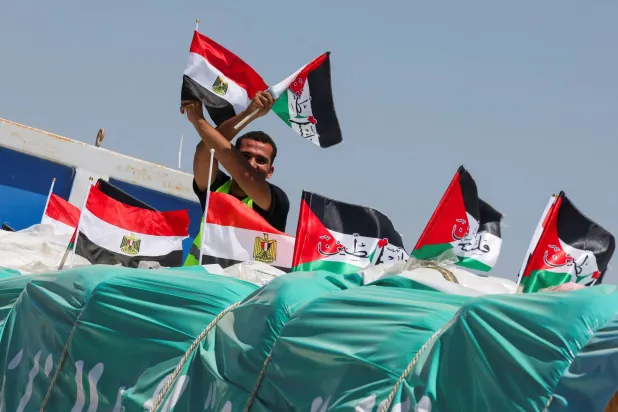 شخص يحمل العلمين المصري والفلسطيني على شاحنة تحمل مساعدات إنسانية بالقرب من معبر رفح (رويترز)