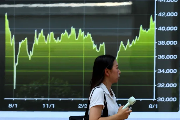 امرأة تسير بجانب شاشة تعرض رسماً بيانياً لتحركات مؤشر «نيكي» للأسهم اليابانية (رويترز)