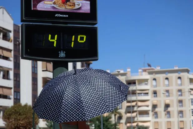 امرأة تمشي بمظلة تحت مقياس حرارة يظهر 41 درجة مئوية وسط موجة حر في قرطبة بإسبانيا (إ.ب.أ)