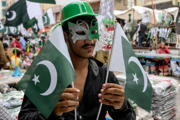 بائع يبيع الأعلام الوطنية الباكستانية يقف لالتقاط صورة له في سوقٍ بكراتشي 12 أغسطس 2025 قبل احتفالات البلاد بيوم الاستقلال (أ.ف.ب)