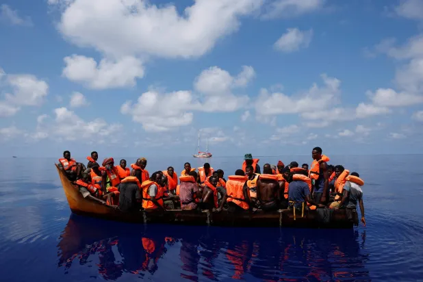 مهاجرون على متن قارب بالقرب من قارب إنقاذ في المياه الدولية جنوب لامبيدوزا في وسط البحر المتوسط... 11 أغسطس 2024 (رويترز)