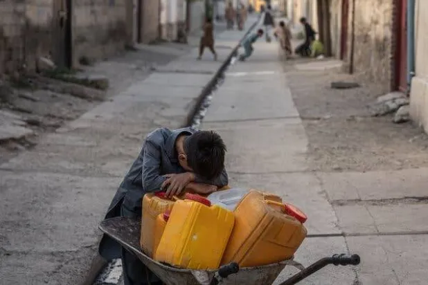 صبي يستريح في طريقه إلى جلب الماء من خارج منزله في كابل بأفغانستان الشهر الماضي (نيويورك تايمز)