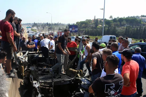 لبنانيون يتفقدون حطام سيارة استهدفتها غارة إسرائيلية جنوب مدينة صيدا (أ.ف.ب)