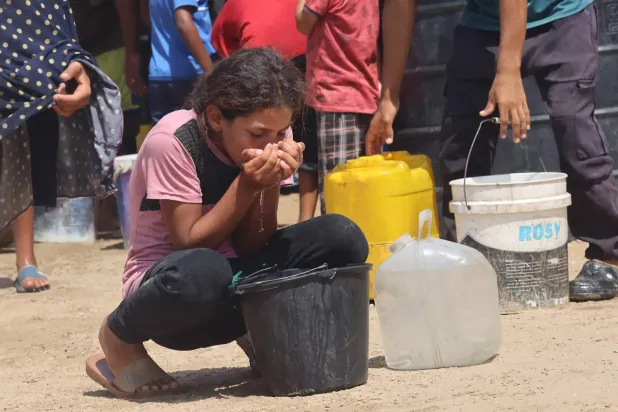 Bir kız çocuğu, dün Gazze Şeridi'nin güneyindeki Han Yunus'ta su arayan Filistinlilerin toplandığı kalabalıkta kovadan su içiyor (AFP)