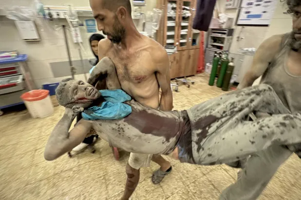 فلسطينيان ينقلان جريحاً أصيب بغارة جوية إسرائيلية على ضاحية الأمل غرب خان يونس الجمعة (د.ب.أ)