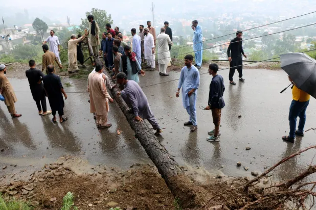 باكستانيون يحاولون رفع شجرة تسد الطريق في مظفر آباد في باكستان (إ.ب.أ)