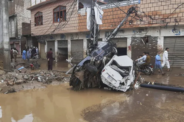 مواطنون يسيرون بجوار سيارات متضررة عالقة في عمود كهرباء بعد فيضانات مفاجئة بسبب الأمطار الغزيرة في أحد أحياء مينجورا - المدينة الرئيسية في وادي سوات شمال غربي باكستان (أ.ب)