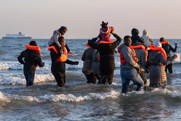 مهاجرون يحملون أطفالهم ويمشون في الماء للصعود على متن قارب مهرّب بمحاولة لعبور القنال الإنجليزي من شمال فرنسا 16 يونيو 2025 (أ.ف.ب)