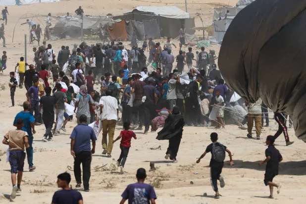 فلسطينيون يركضون نحو مساعدات أُسقطت جواً في دير البلح وسط قطاع غزة (رويترز)