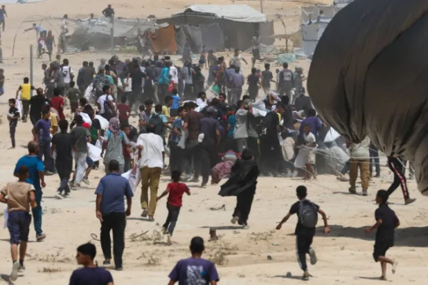 فلسطينيون يركضون نحو مساعدات أُسقطت جواً في دير البلح وسط قطاع غزة (رويترز)
