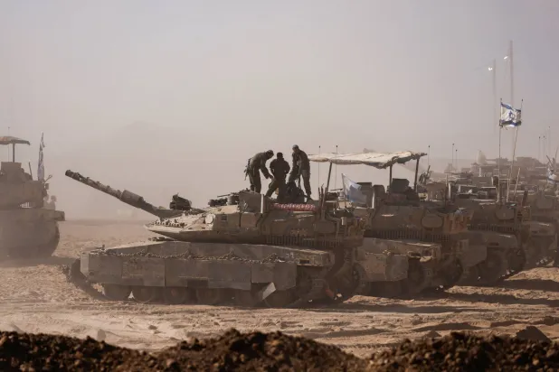 جنود إسرائيليون فوق دبابة كما شوهدوا من الجانب الإسرائيلي للحدود مع غزة (رويترز)