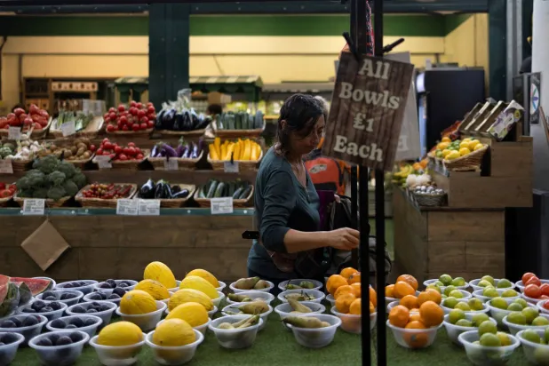 امرأة تشتري الفواكه والخضراوات في السوق المحلي بمدينة برايتون (رويترز)