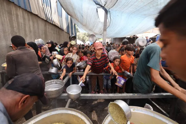 فلسطينيون يتجمعون لتسلم وجبات طعام مطبوخة من مركز توزيع أغذية في مخيم النصيرات للاجئين وسط قطاع غزة (أ.ف.ب)