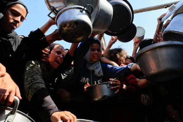 فلسطينيون يحملون أواني الطعام في انتظار الحصول على الطعام من مطبخ خيري في خان يونس جنوب قطاع غزة (رويترز)