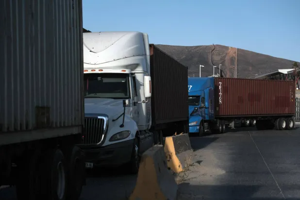 شاحنات تصطف بجانب الجدار الحدودي قبل عبورها من المكسيك إلى الولايات المتحدة (أ.ف.ب)