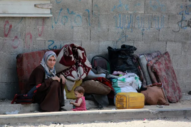 امرأة فلسطينية مع رضيعتها تجلسان في الشارع بجانب أمتعتهما في مدينة غزة (أ.ف.ب)